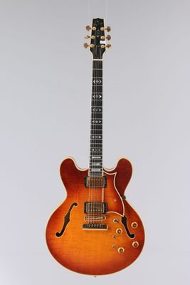 une guitare électrique orange suspendue à une ficelle sur un mur blanc