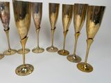 six gold wine glasses lined up in a row on a white surface