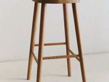 un tabouret en bois avec une assise en bois posé sur un sol blanc