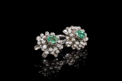 une paire de boucles d'oreilles en émeraude et diamant posées sur un fond noir
