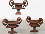 trois urnes anciennes en fonte posées sur des socles dans une pièce