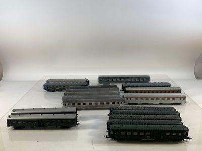 Plusieurs trains miniatures sont alignés sur une table devant un fond blanc.