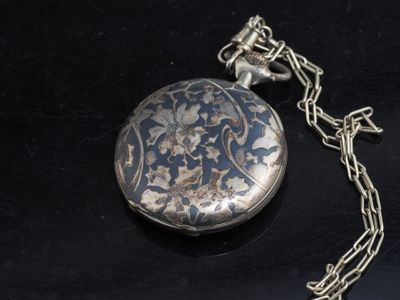 une montre de poche en argent attachée à une chaîne, posée sur une surface noire