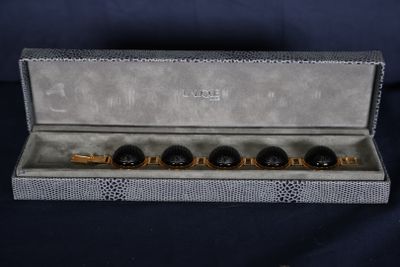 une photo d'un lot de quatre boutons de manchette noirs et dorés dans un coffret