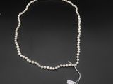 un collier de perles blanches muni d'un fermoir en argent, sur fond noir