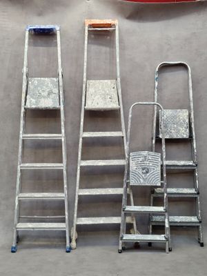 several ladders and a chair are lined up against a wall