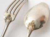 two silver spoons and a fork on a white surface
