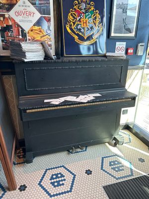 un piano dans un coin d'une pièce où sont accrochés des tableaux au mur