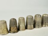 six dés à coudre anciens alignés sur une surface blanche