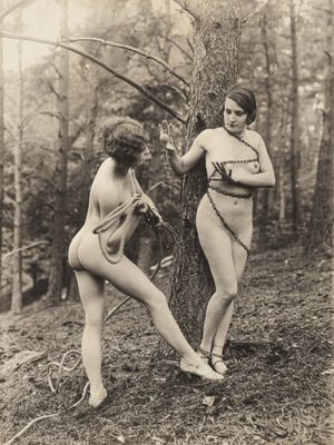 une vieille photo montrant deux femmes debout près d'un arbre dans les bois