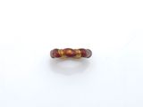 une image représentant une bague rouge et dorée posée sur une surface blanche