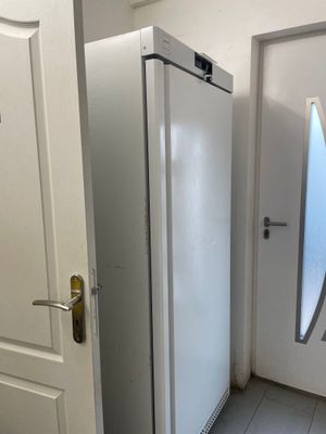 un réfrigérateur blanc dans un coin de la pièce, près d'une porte