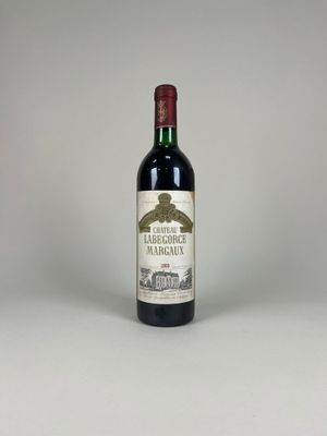 une bouteille de vin rouge posée sur une table blanche, sur fond gris