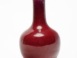 un vase rouge posé sur une surface blanche