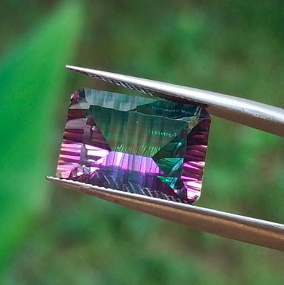un gros plan d'une pierre précieuse violette et verte tenue par une paire de pinces