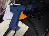 un pistolet à colle bleu posé sur un bureau, à côté d'une feuille de papier