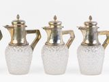 quatre vases en verre et un vase en argent posés sur une surface blanche