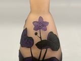 a vase with a purple flower on it on a white surface