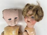 two old dolls sitting next to each other on a white surface