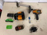 des outils disposés sur une table, notamment un niveau laser, un marteau, une batterie, un chargeur et un cordon d'alimentation