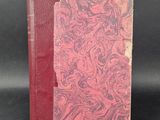 an old book with a red cover sitting on top of a black surface