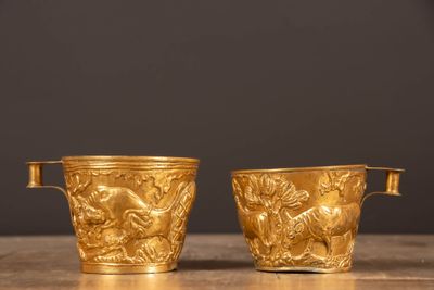 une paire de vases plaqués or posés sur une table en bois, sur fond noir