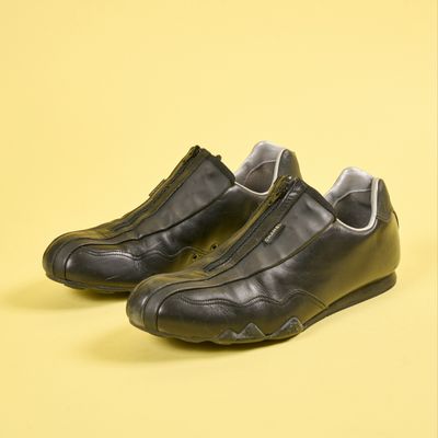une paire de chaussures en cuir noir avec des fermetures éclair, sur fond jaune