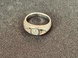 une bague en argent avec une pierre au centre, posée sur un tissu