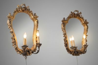 pair of gilded mirrors with candles on a stand in front of a gray wall