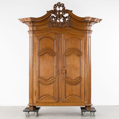 une armoire ancienne en bois, avec un dessus sculpté, montée sur roulettes