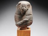 une statue en pierre représentant un sphinx posée sur un bloc de bois