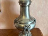 a silver vase sitting on a wooden table with a lamp on it