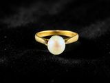 a gold ring with a white pearl on a black background