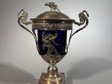 a silver and blue vase on a stand with a bird on it