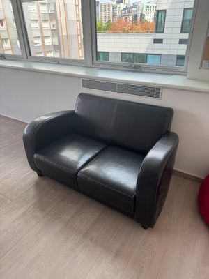 a black leather couch sitting in front of a window in a living room