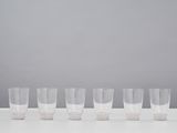 six clear glasses lined up in a row on a white table