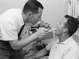 photographie en noir et blanc d'un homme en train de se faire brosser les dents par un dentiste