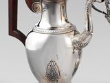 une théière ancienne en argent, munie d'une poignée en bois et posée sur un socle