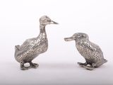 une paire de figurines de canards en argent sur fond blanc
