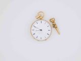 a gold pocket watch and a gold key on a white surface