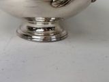 a silver bowl on a white table with a flower in it