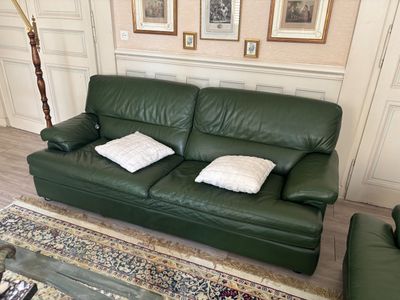 a green leather couch in a living room with pictures on the wall
