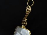 a close up of a gold plated pendant with a white stone
