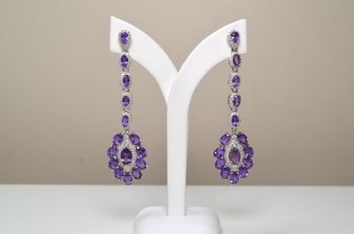 des boucles d'oreilles violettes et blanches posées sur un présentoir blanc, sur une table blanche