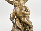 une statue antique en bronze représentant un Cupidon tenant un oiseau, posée sur un socle en bois