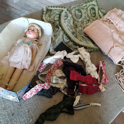 une poupée posée dans un panier posé par terre, à côté d'autres objets