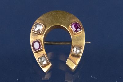 une image représentant une broche en forme de fer à cheval en or, sertie de pierres précieuses