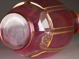 a red glass vase with a gold decoration on it