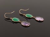 a pair of earrings with green and purple stones on a black surface