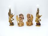 three gold figurines of angels and a lamp on a white background